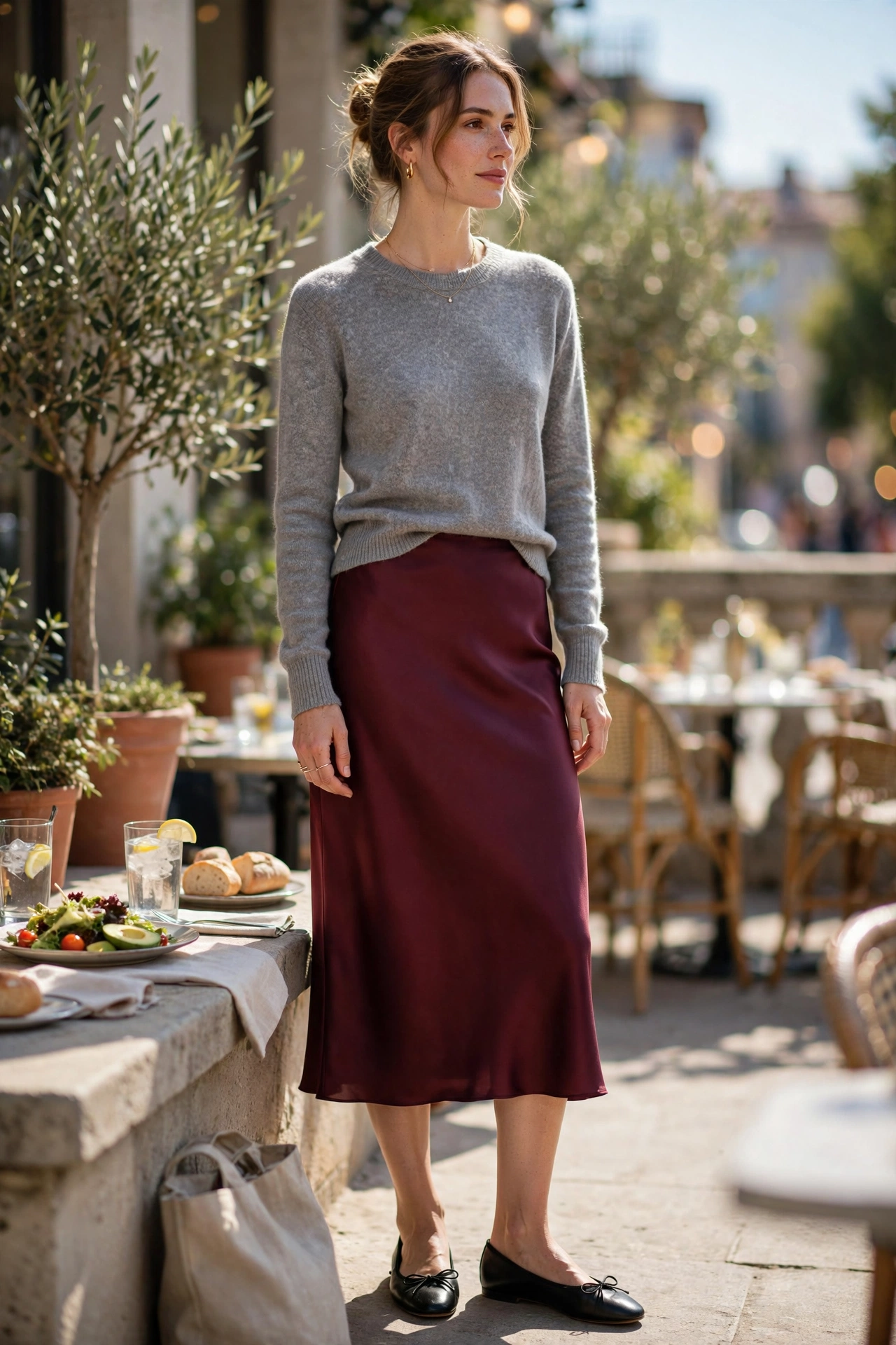 Woman in a burgundy silk slip skirt and a grey crewneck knit with black ballet flats